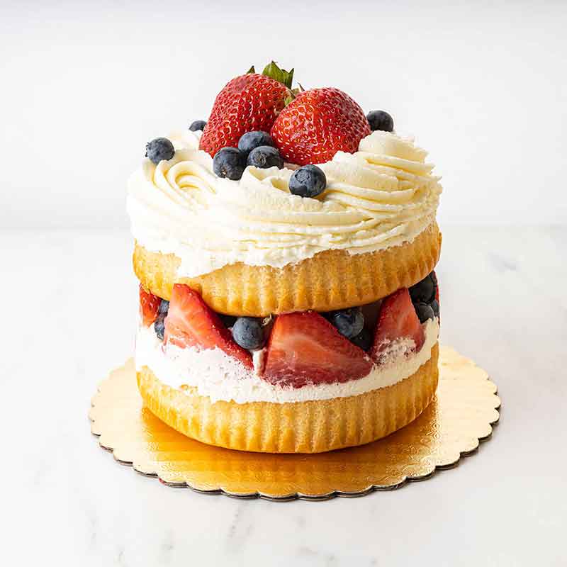 A two-layer strawberry shortcake with whipped cream, strawberries and blueberries