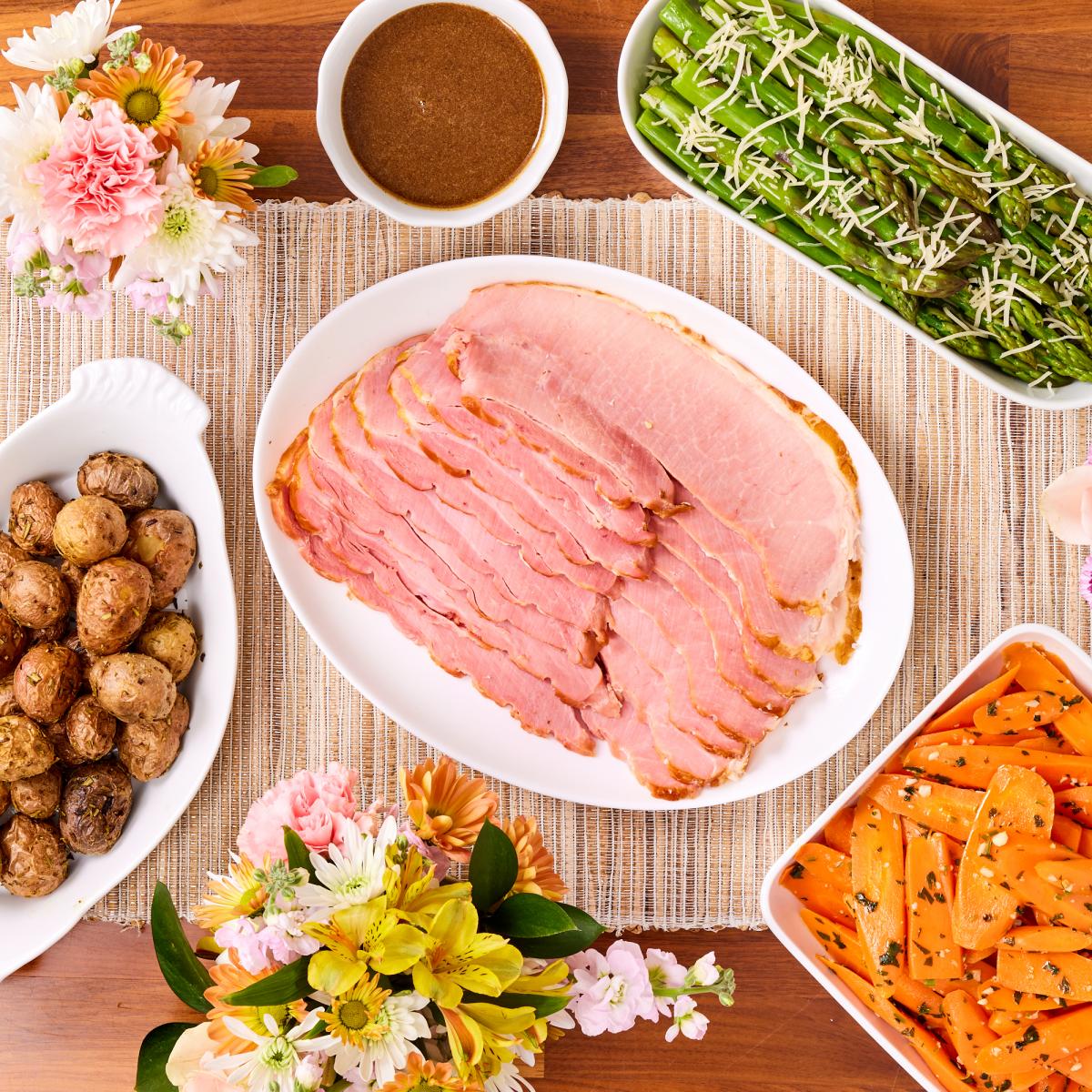 table with ham, glaze, carrots, asparagus and potatoes with spring colored flowers