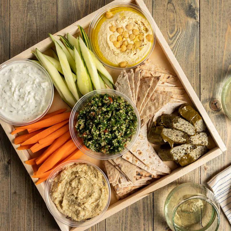 A tray of hummus, baba ganoush, tzatziki, flatbread triangles, tabbouleh, dolmas and crudités
